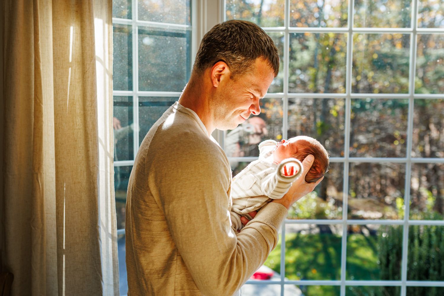 Newborn photography dad holding baby by window