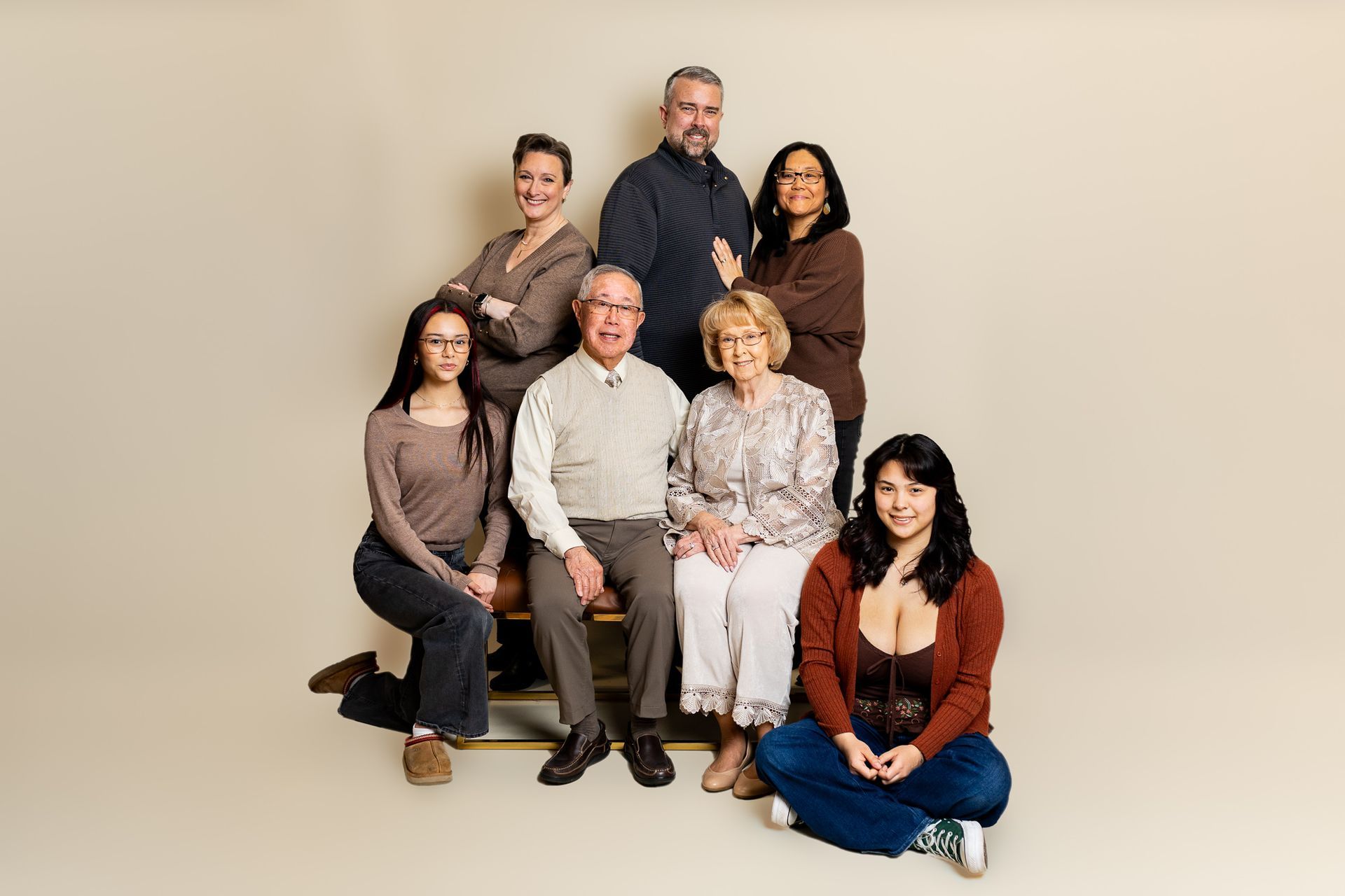Seven people posing in a studio, seated and standing against a beige background. - family photos