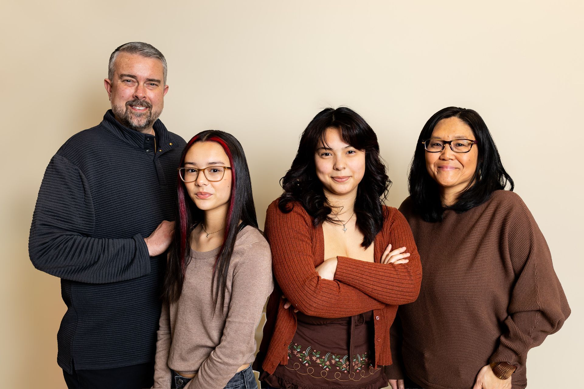 Four people posing together against a plain beige backdrop, with two smiling and two standing with arms crossed. - family photos