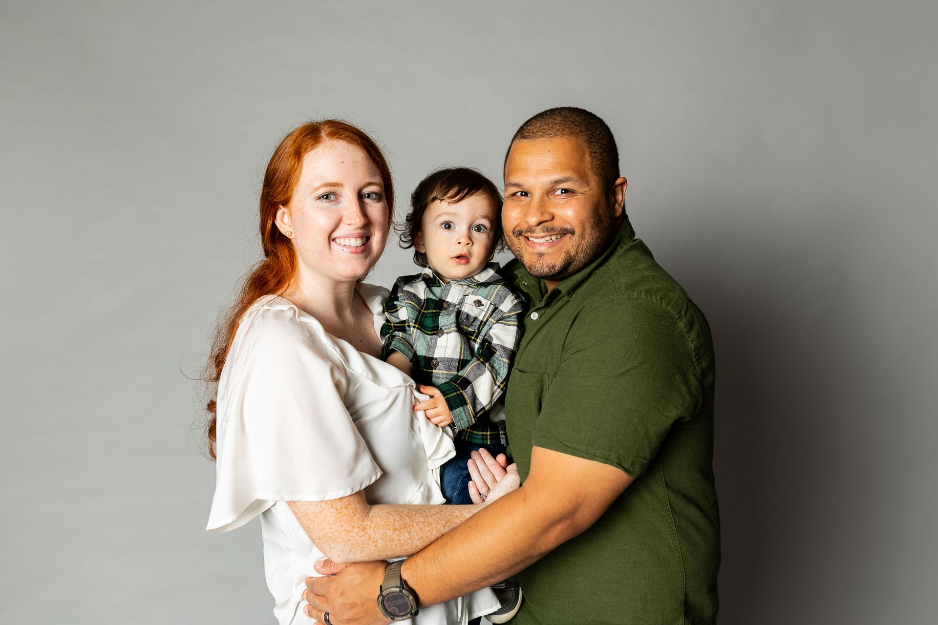Family portrait of three people posing together against a gray studio backdrop - family photos