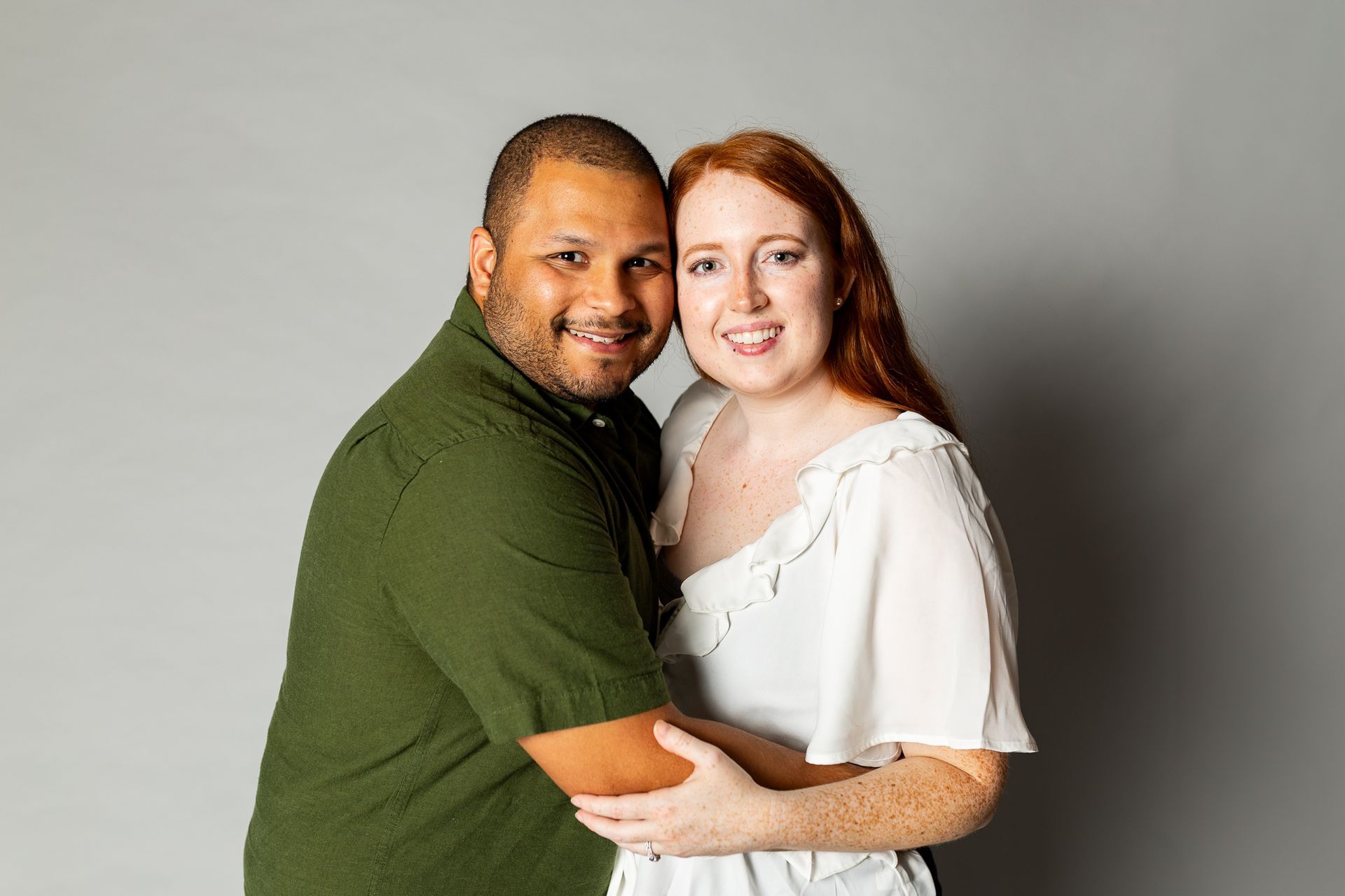 Two adults smiling and embracing against a plain gray background - family photos