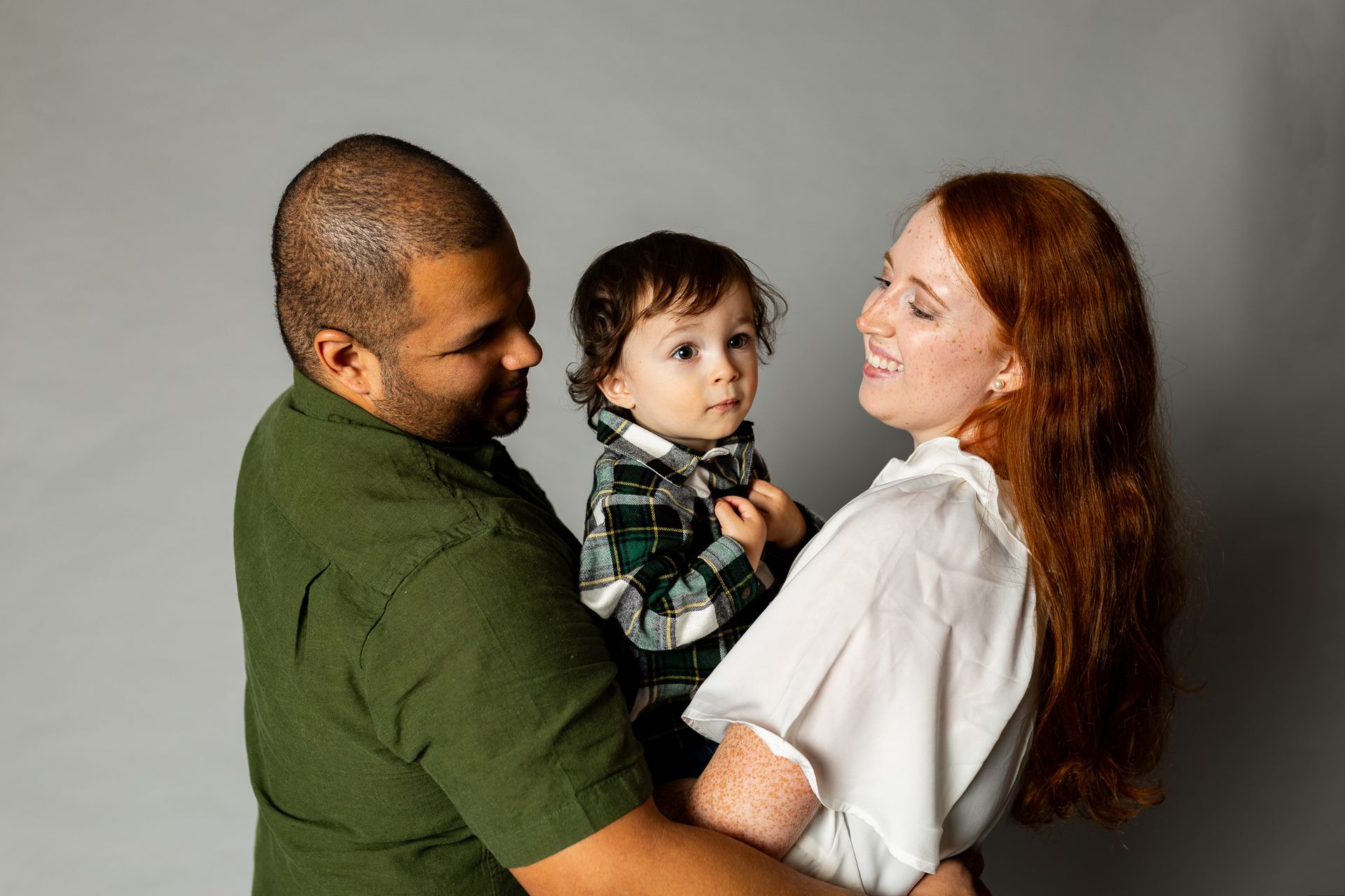 Three people in a studio, a smiling adult holding a child, with another adult facing them. - family photos