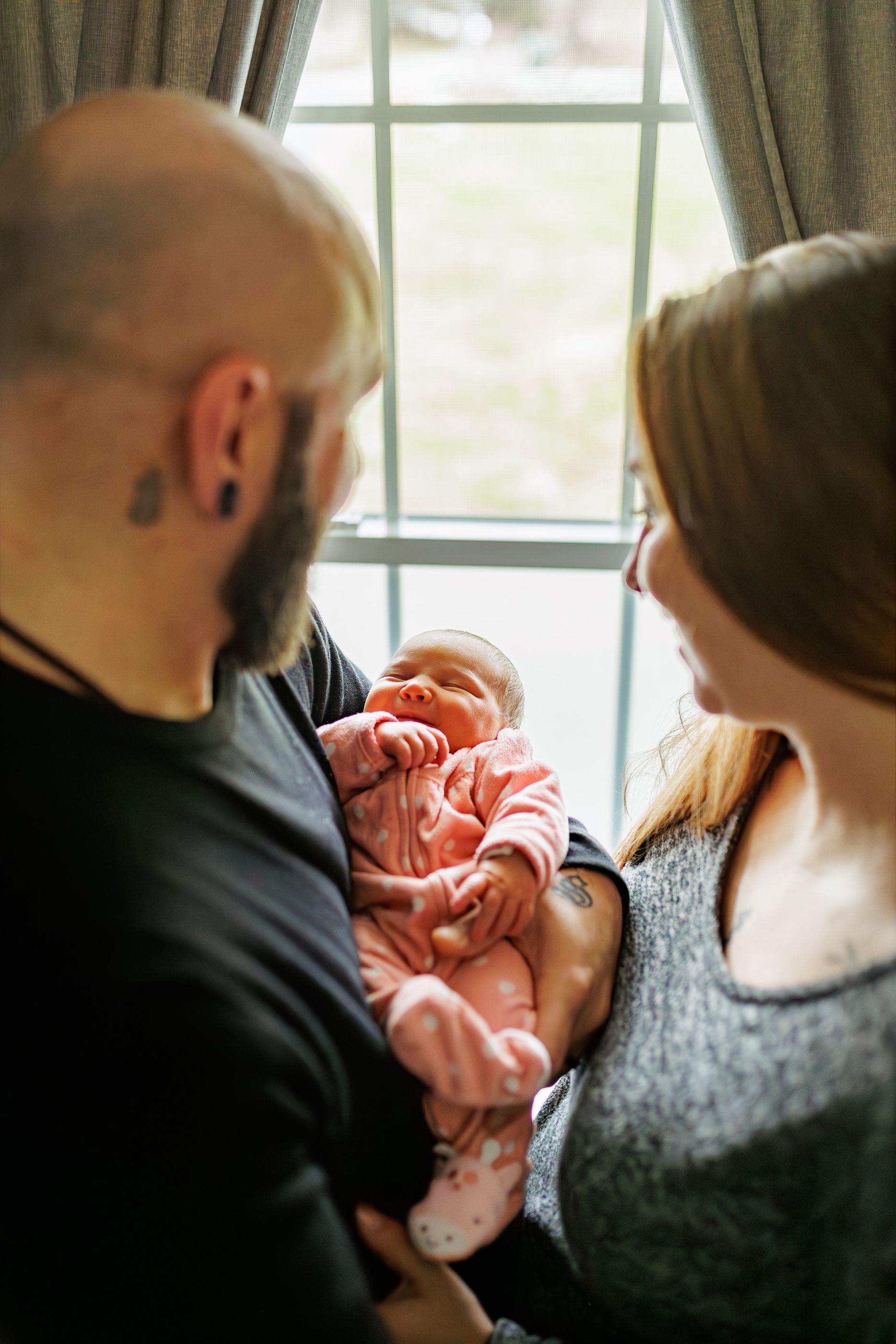 Newborn photography mom and dad holding baby by window
