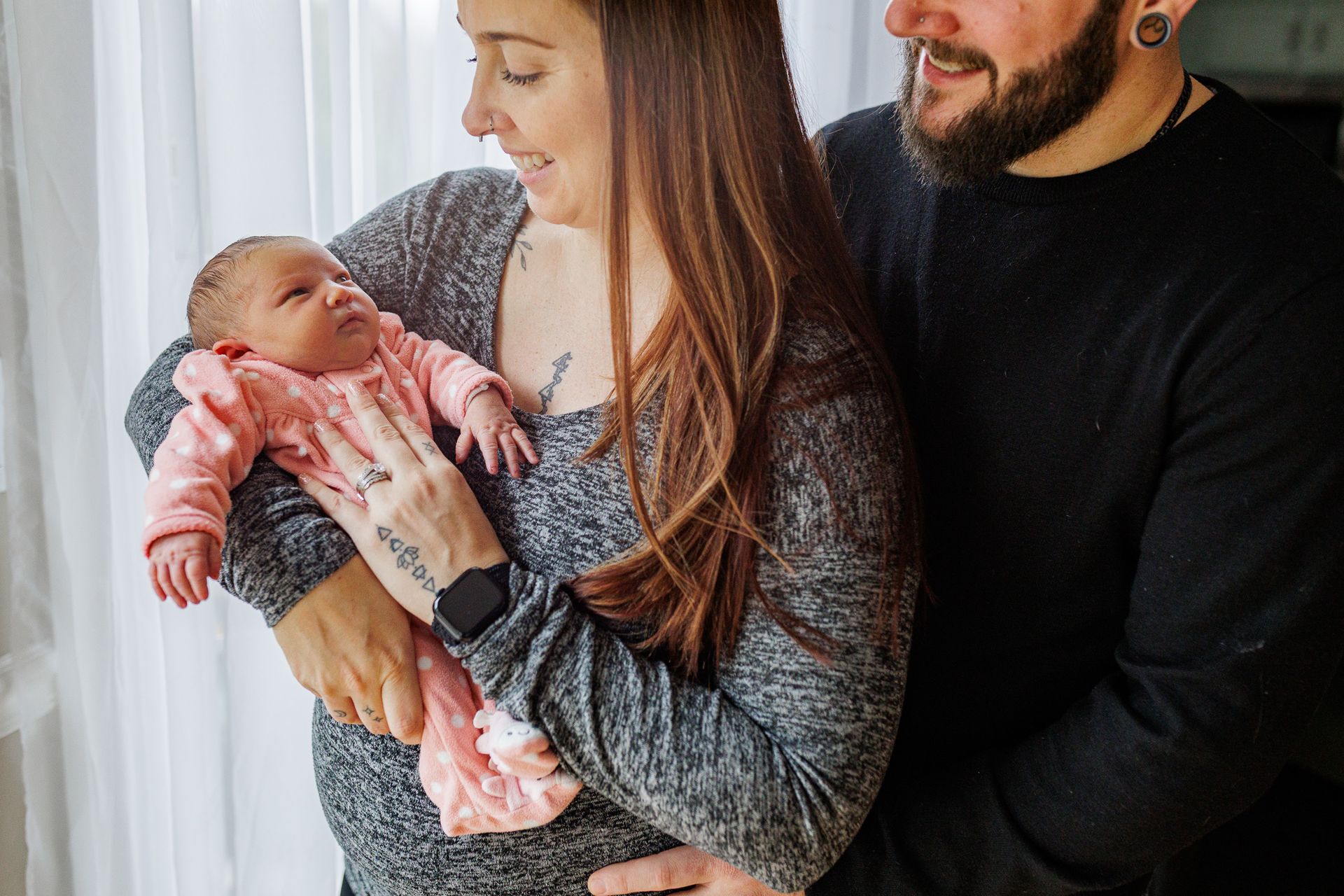 parents holding newborn by window during newborn session