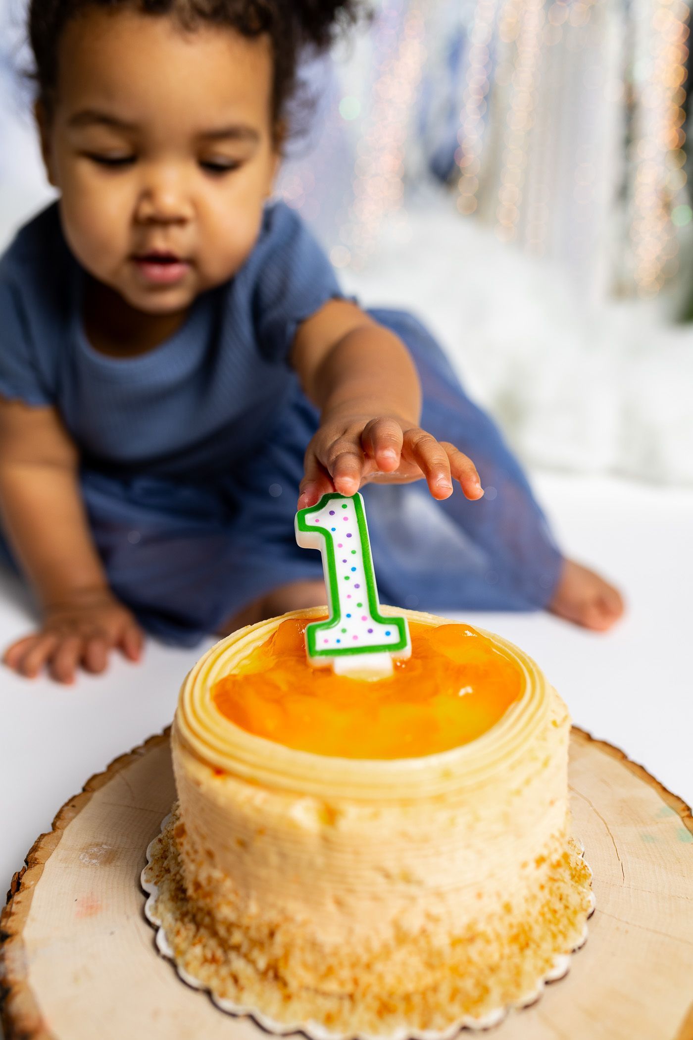 baby reaching for candle in a winter themed studio set with snowy background, mini christmas trees, and santa for cake smash session