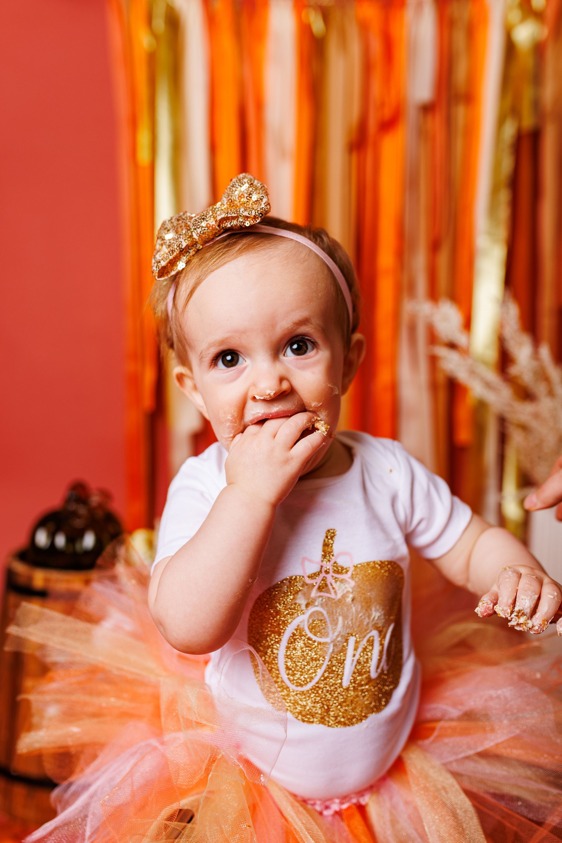 baby standing in a fall themed studio set with ribbons, pumpkins, leaves and streamers for cake smash session