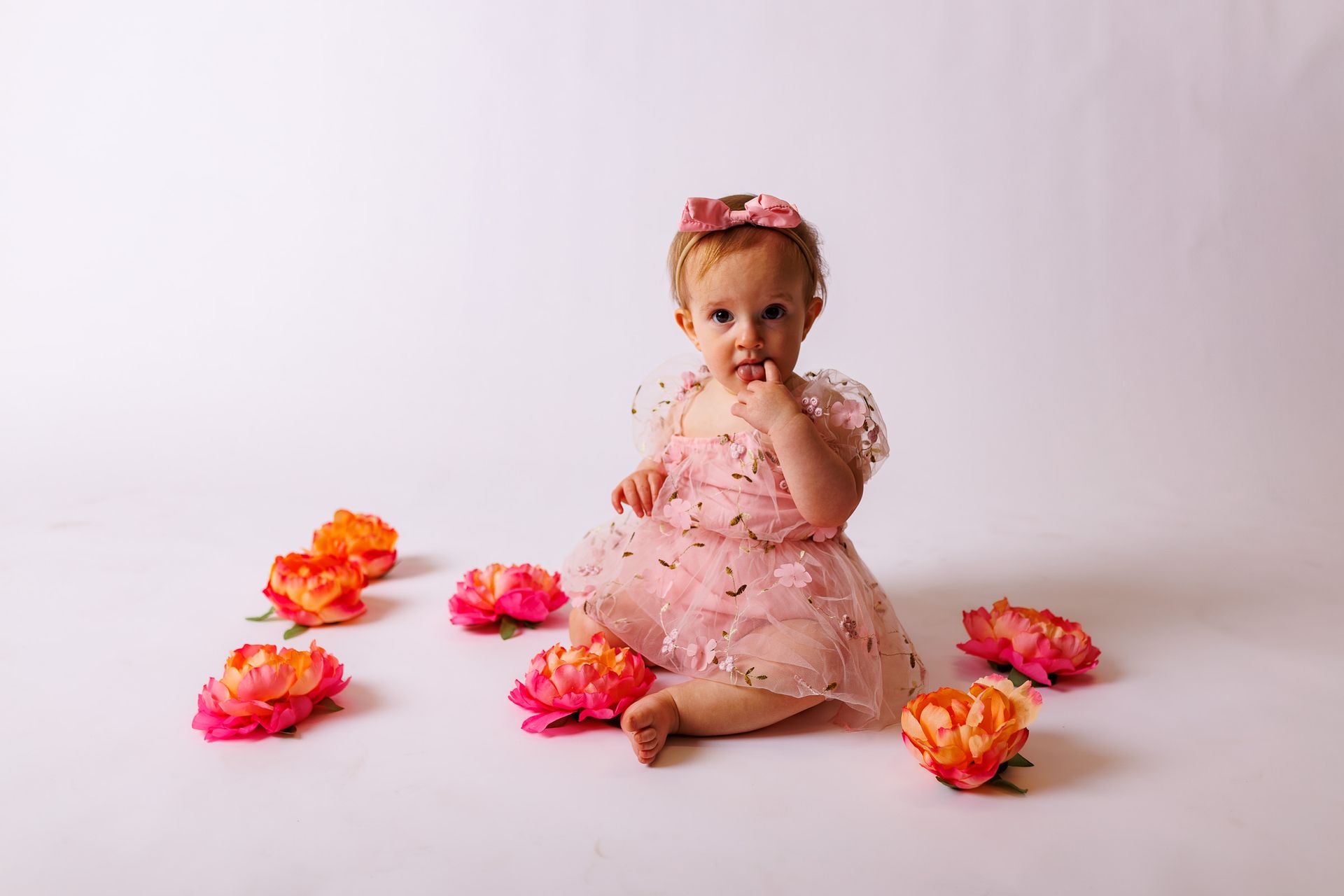 Baby posing on white background with orange and pink flowers for cake smash session