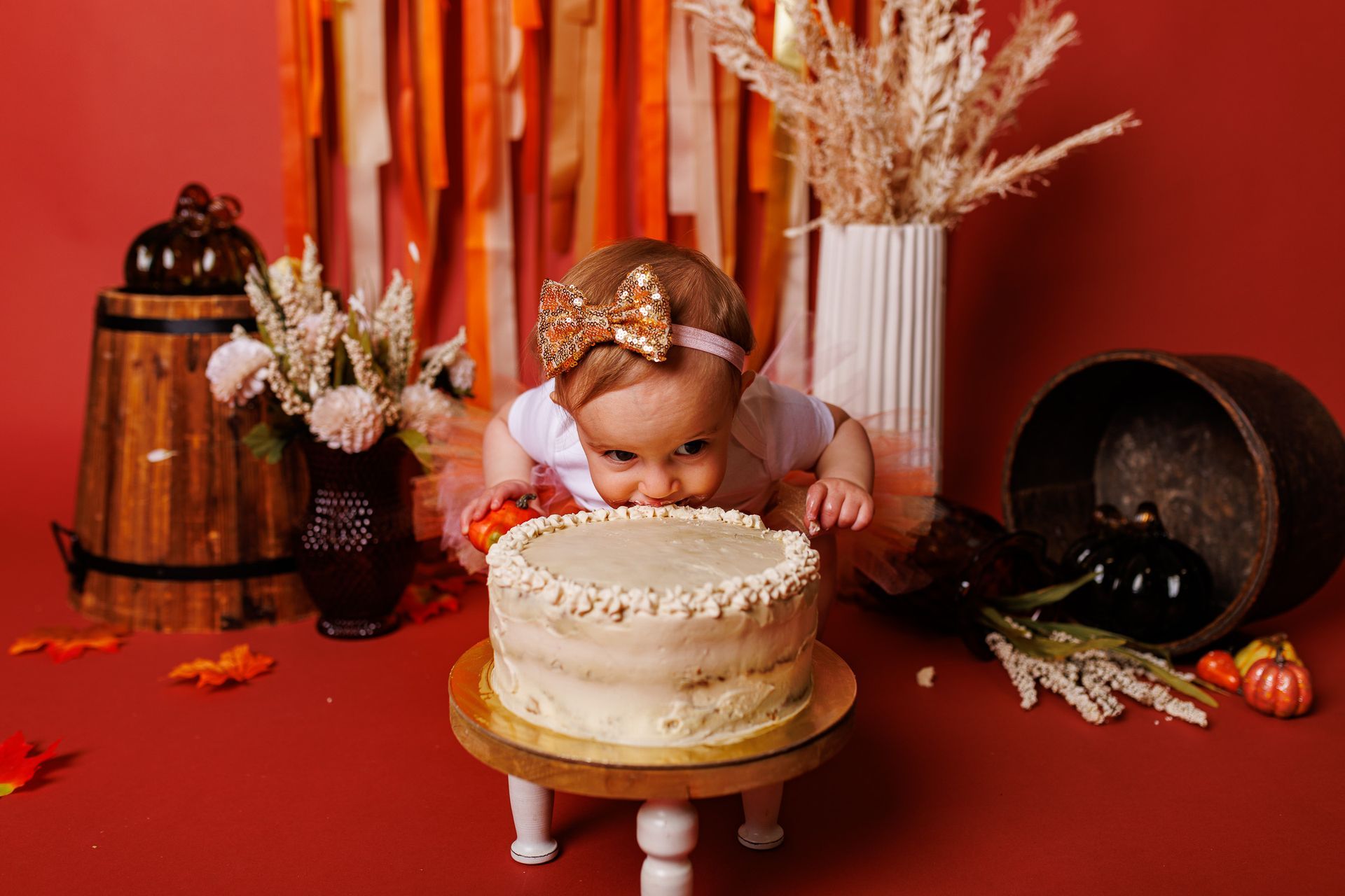baby standing in a fall themed studio set with ribbons, pumpkins, leaves and streamers for cake smash session