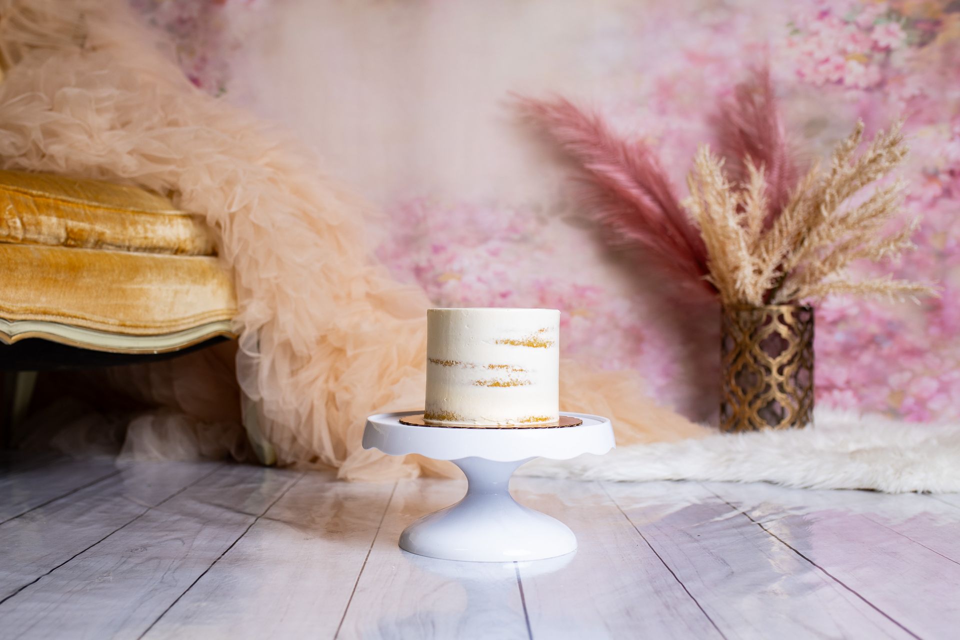 A small cake is sitting on a white cake stand in a room.