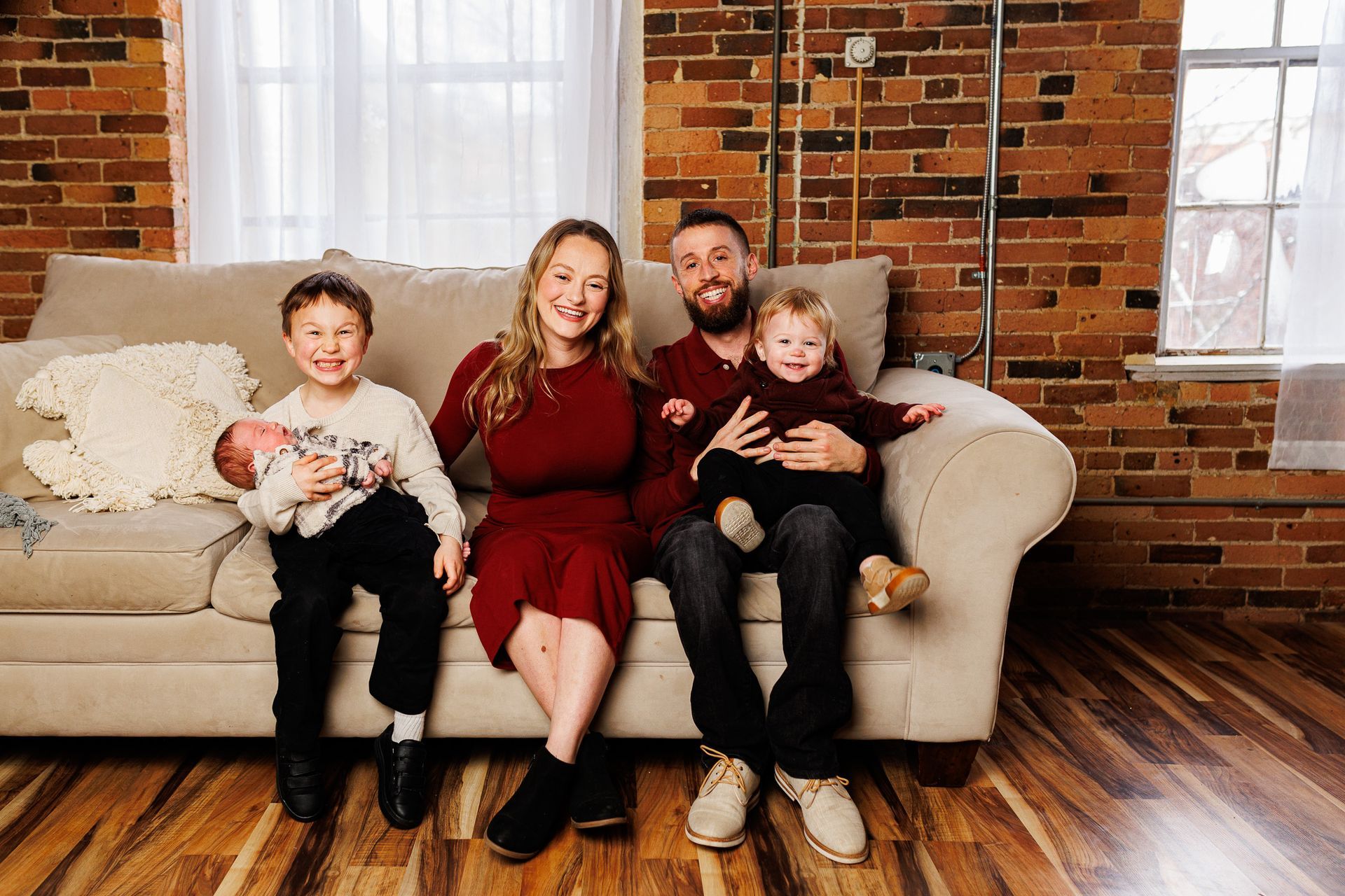 Family of four sitting on a couch in a brick-walled living room, smiling at the camera. - family photos