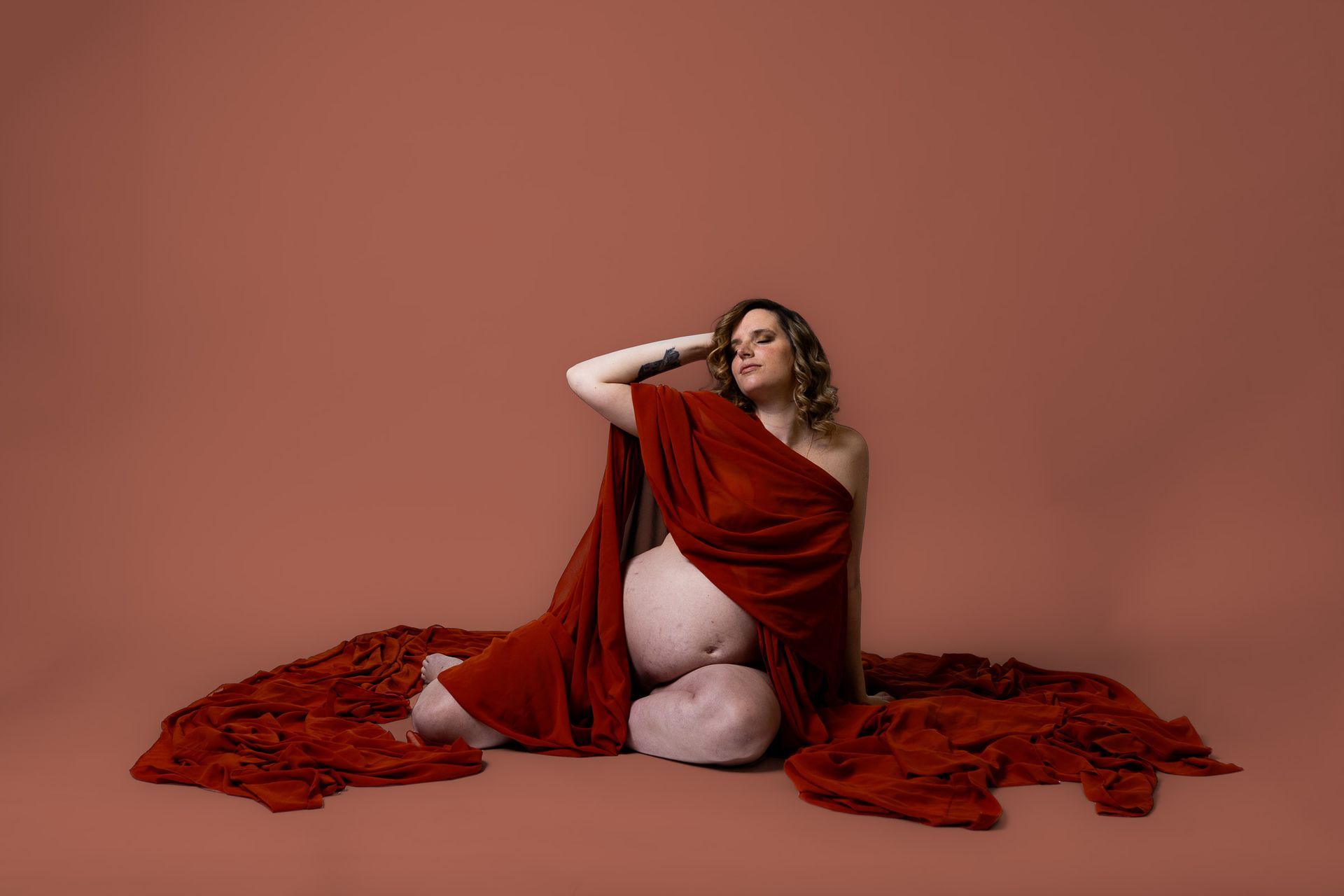 Maternity photography mom posing on red background in long drapes