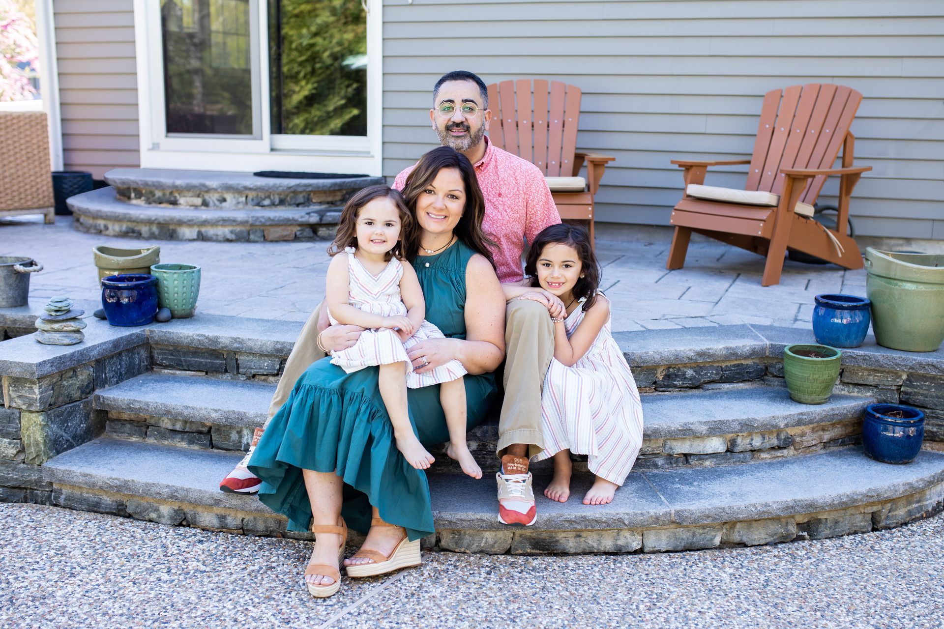 Family sitting on stone steps on a porch, smiling with two children and a pet beside them. - family photos