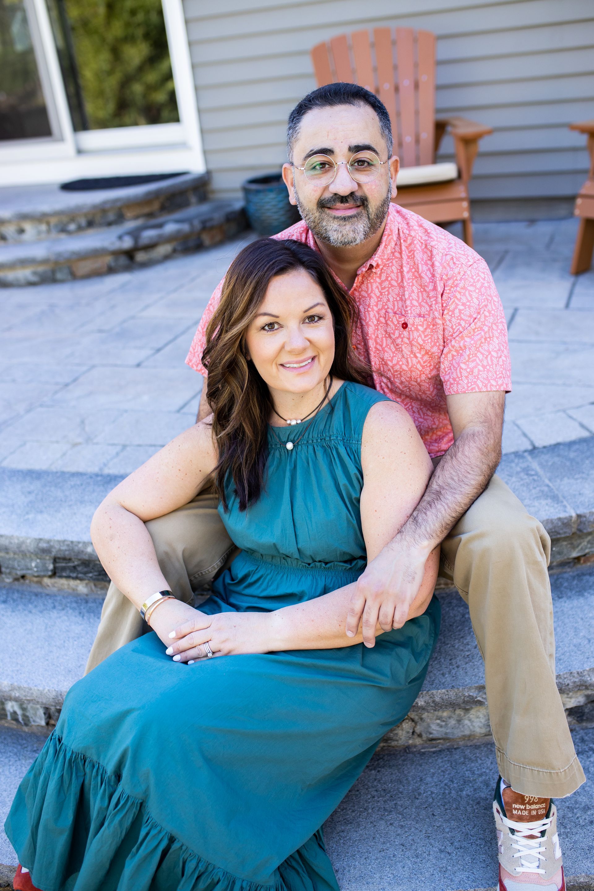 Couple sitting on outdoor steps, smiling, with a porch and chair behind them - family photos