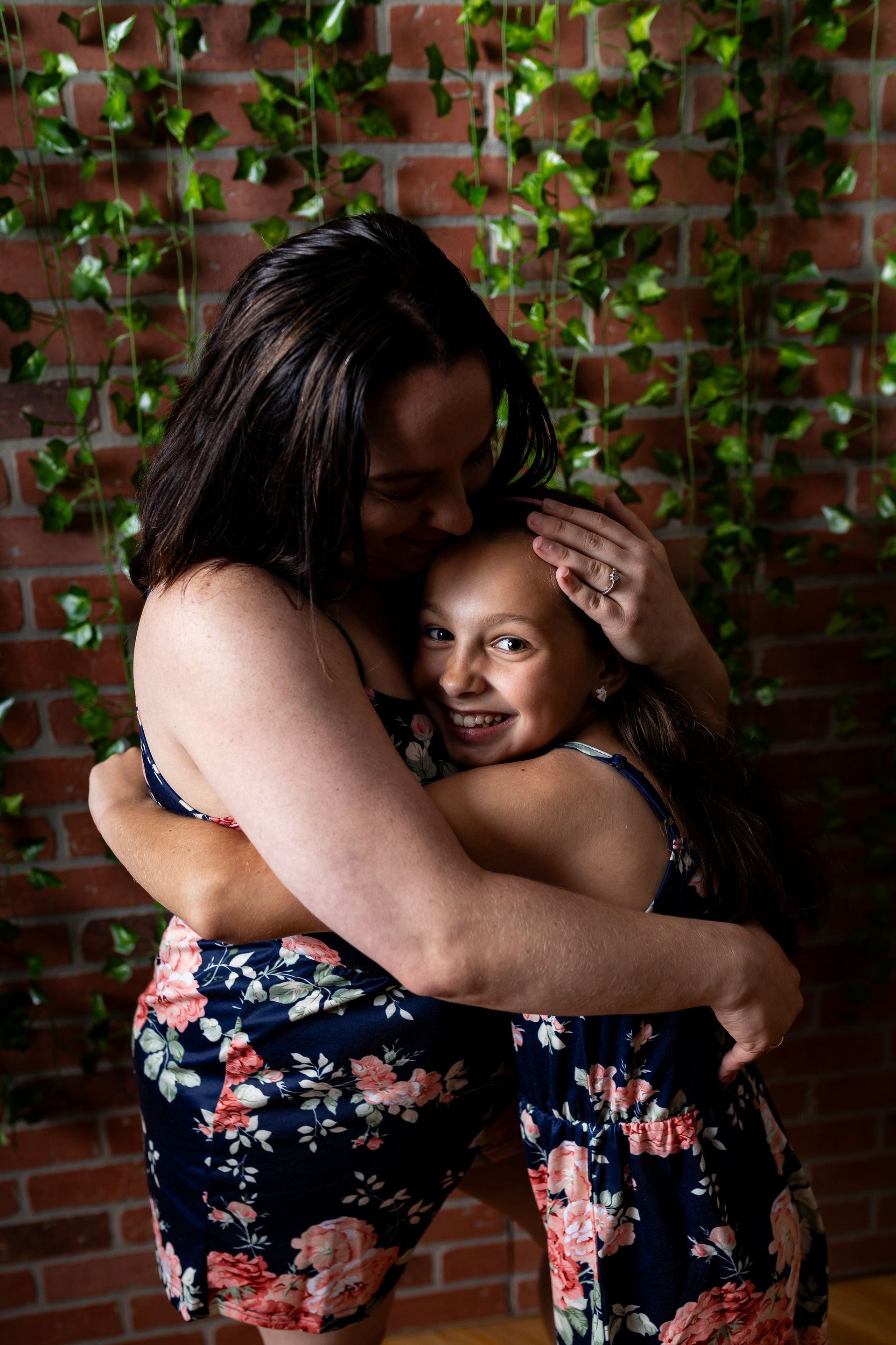 A woman is hugging a little girl in front of a brick wall.