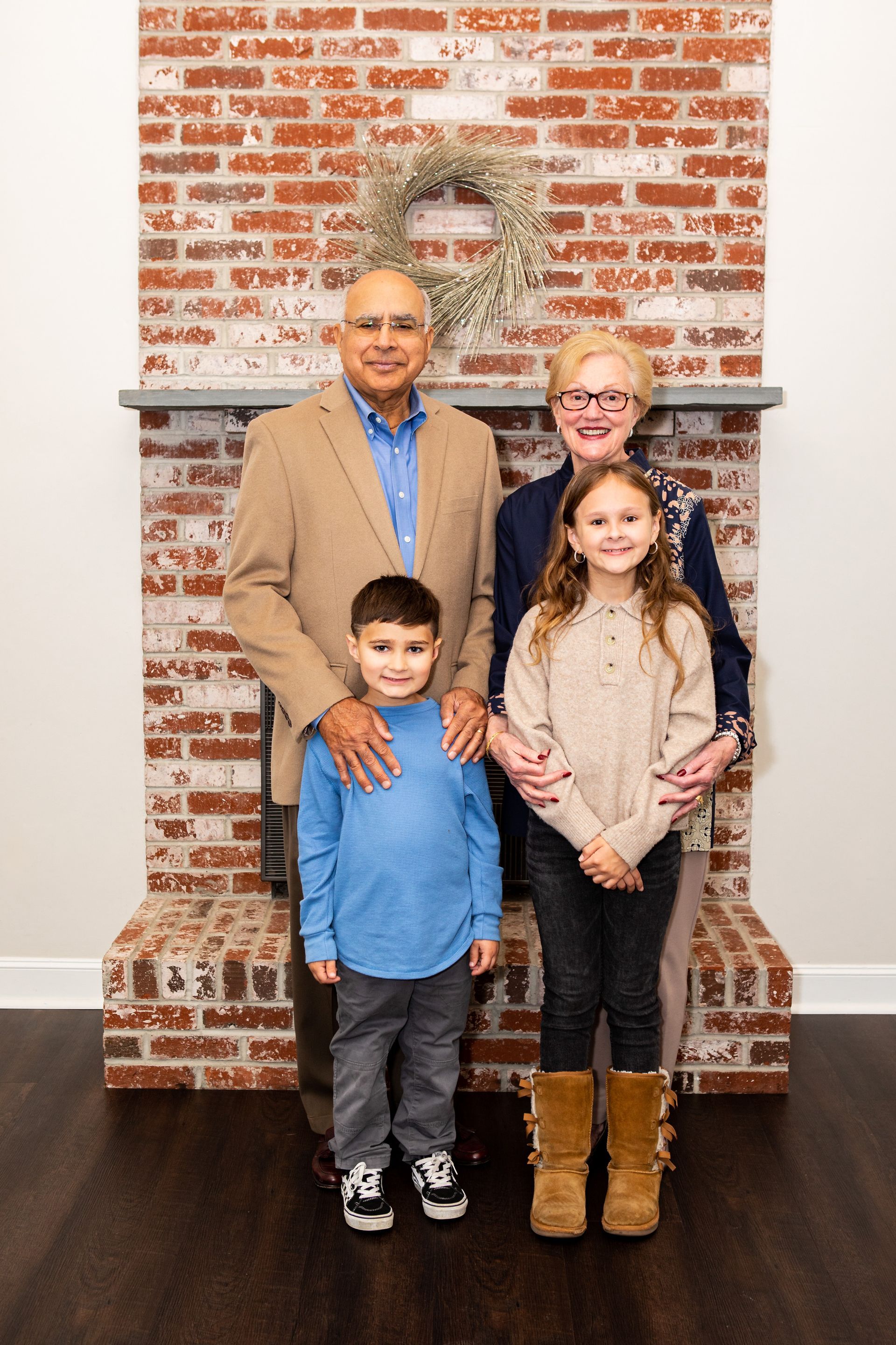 Family of four posing indoors in front of a brick wall, with a large portrait behind them. - family photos