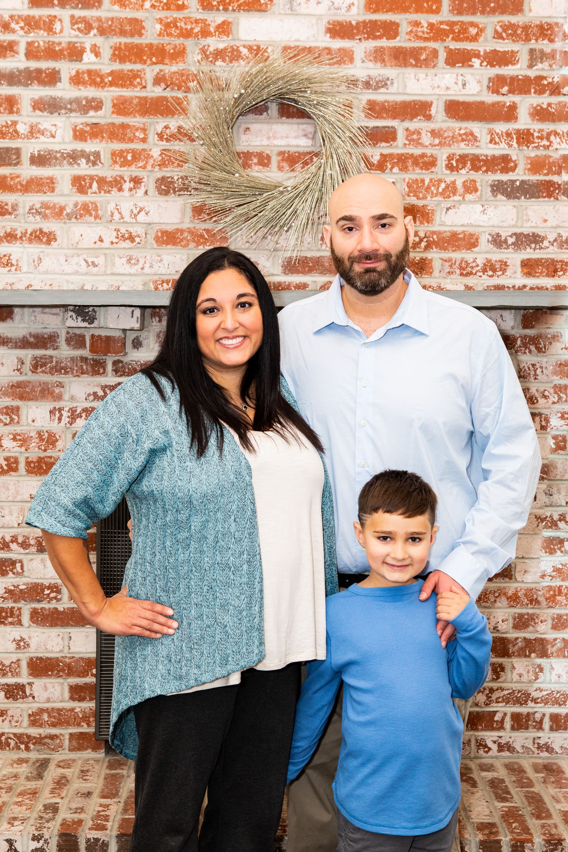 Three people posing in front of a brick wall, with two adults and a child in blue and white clothing. - family photos