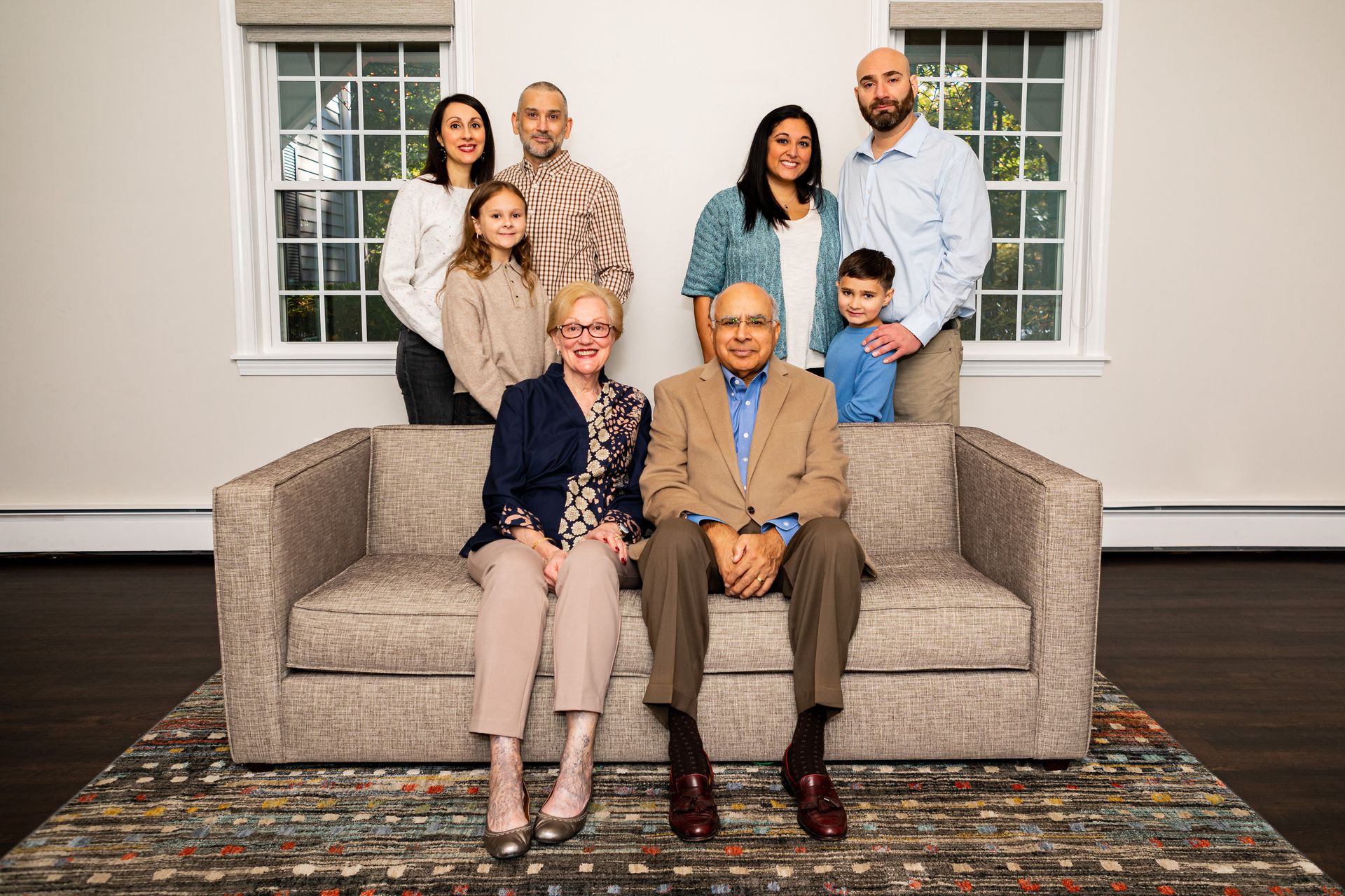 Family portrait with seven people posed around a beige couch in a bright living room. - family photos