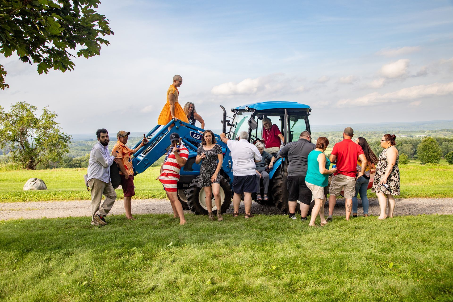 People gathered around a tractor carrying a statue in a grassy field under a cloudy sky. - family photos