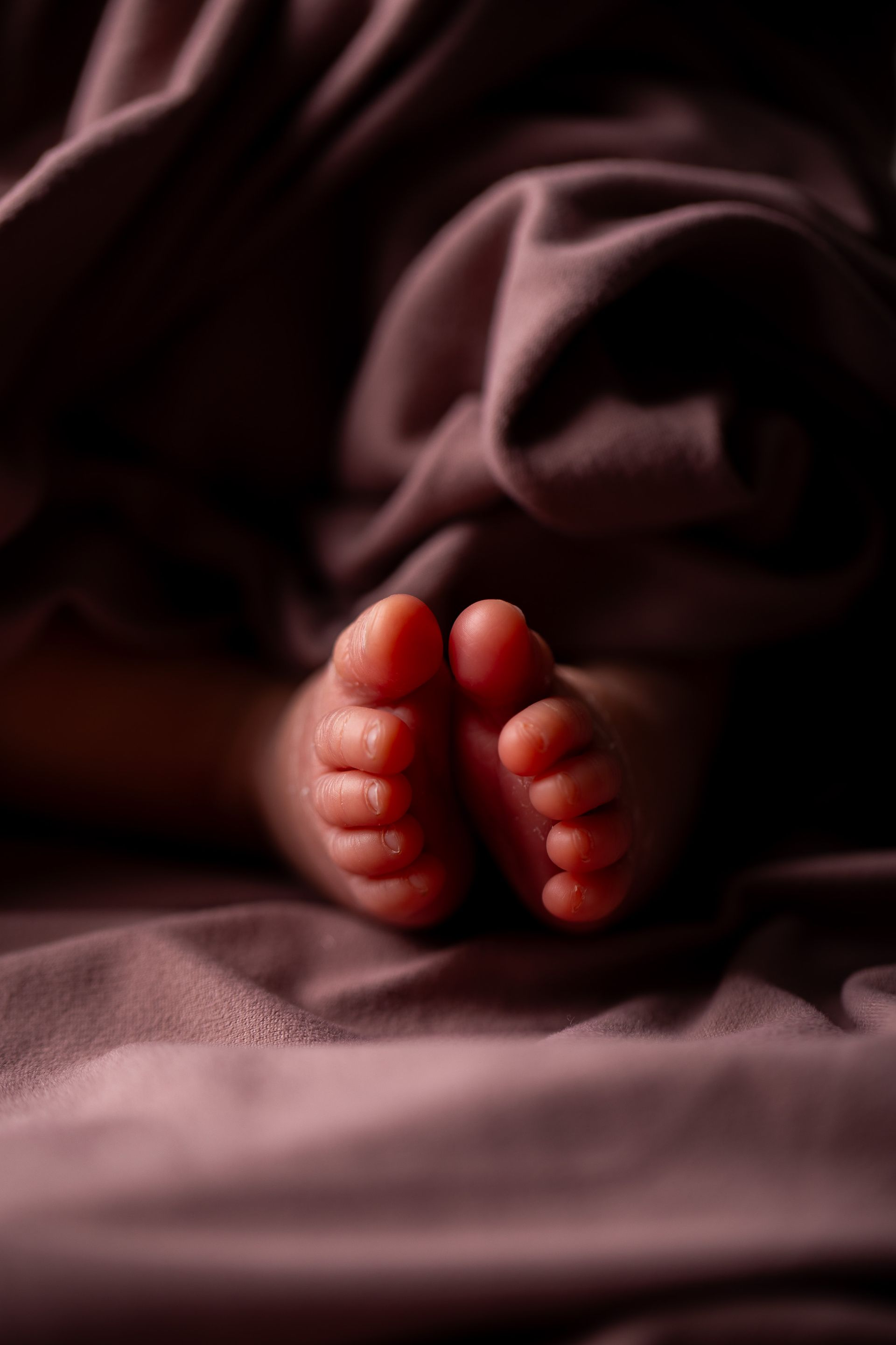 Bare feet resting on dark rumpled fabric, softly lit in warm red tones