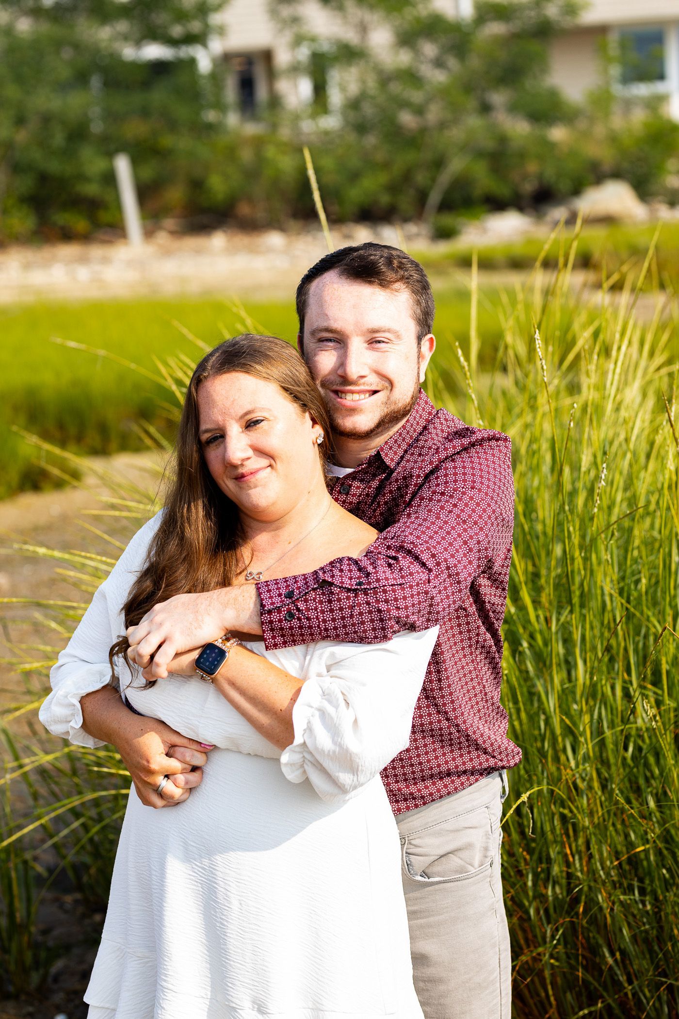 Couple embracing during engagement session on the beach in front of tall grass