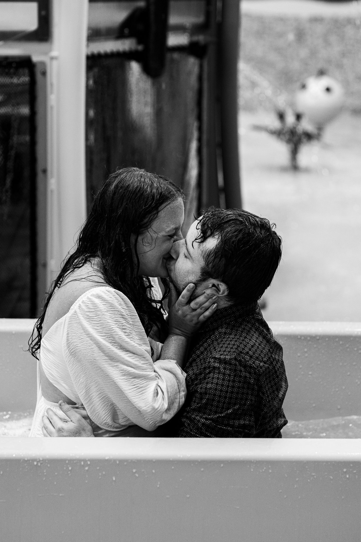 Couples sitting while in water during engagement session on splash pad