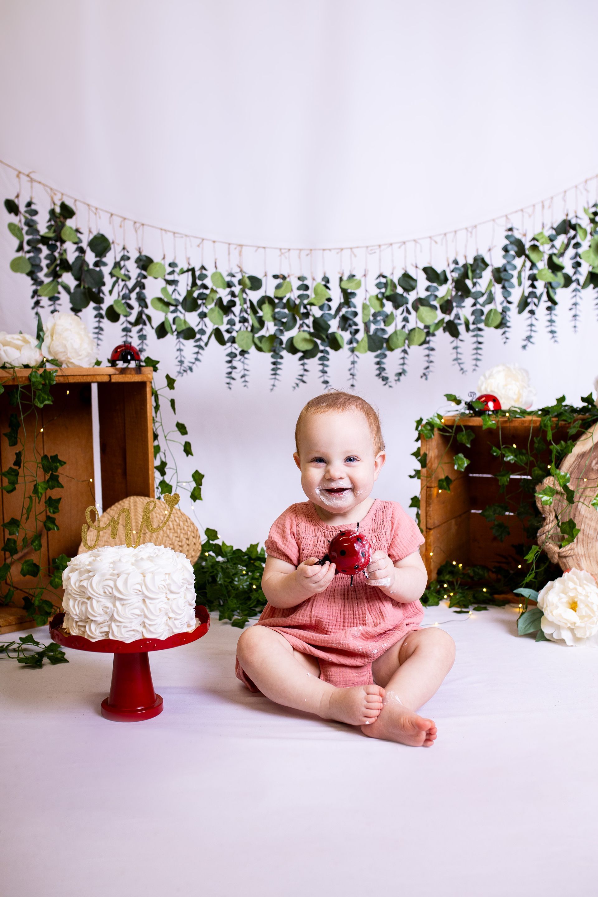 Baby posing on white background for ladybug themed cake smash session