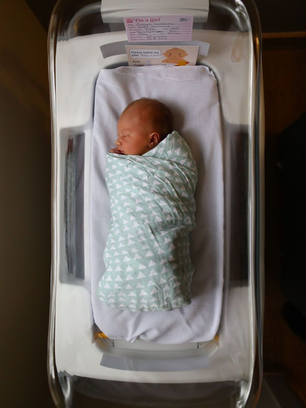 A newborn baby wrapped in a blanket is sleeping in a hospital bed.