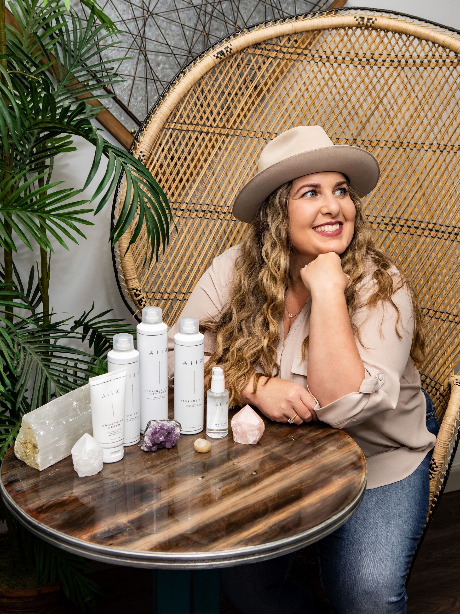 Photography MA -A woman in a hat is sitting at a table with bottles of cosmetics.