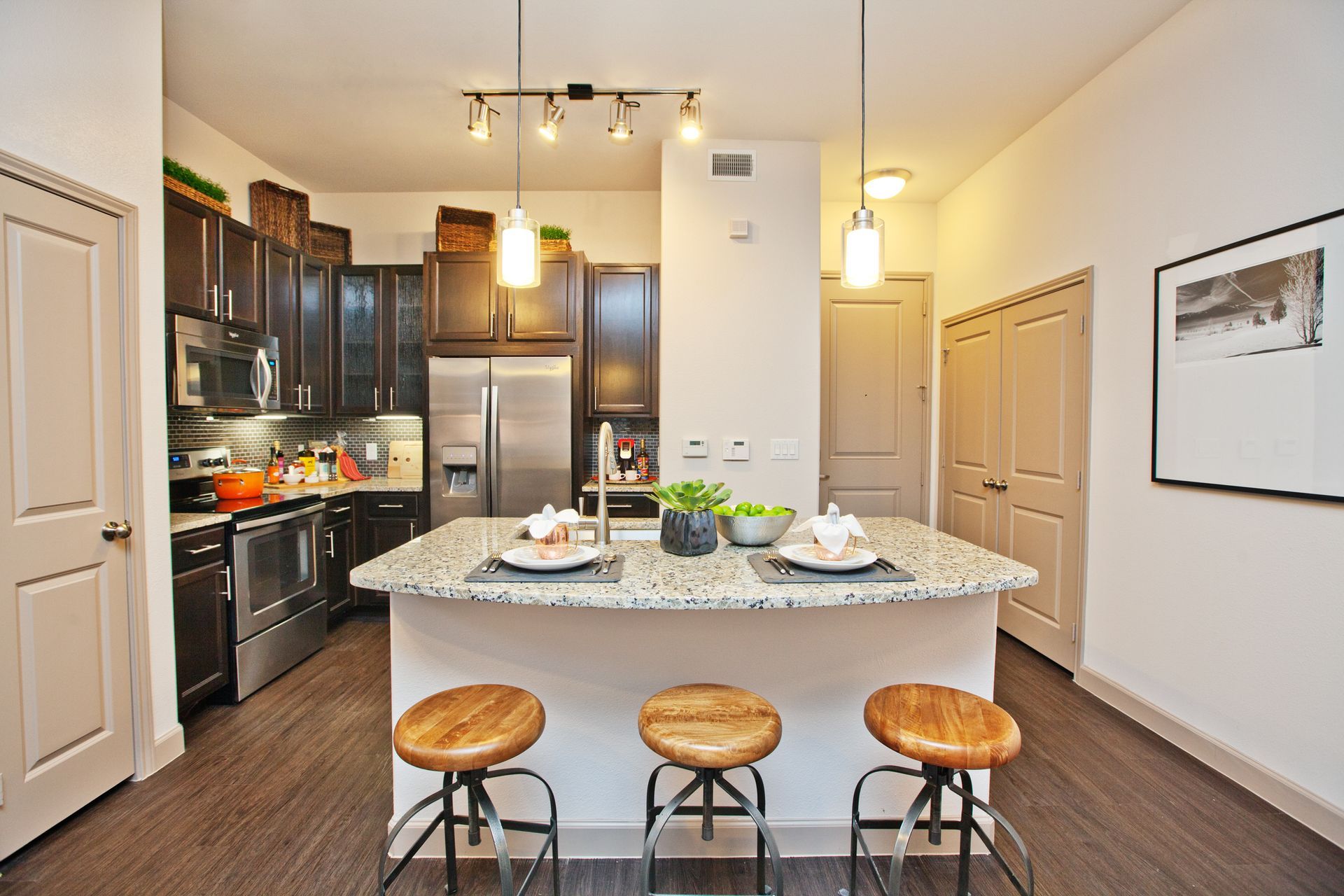 Modern kitchen with granite island, dark wood cabinets, stainless appliances, and three stools.