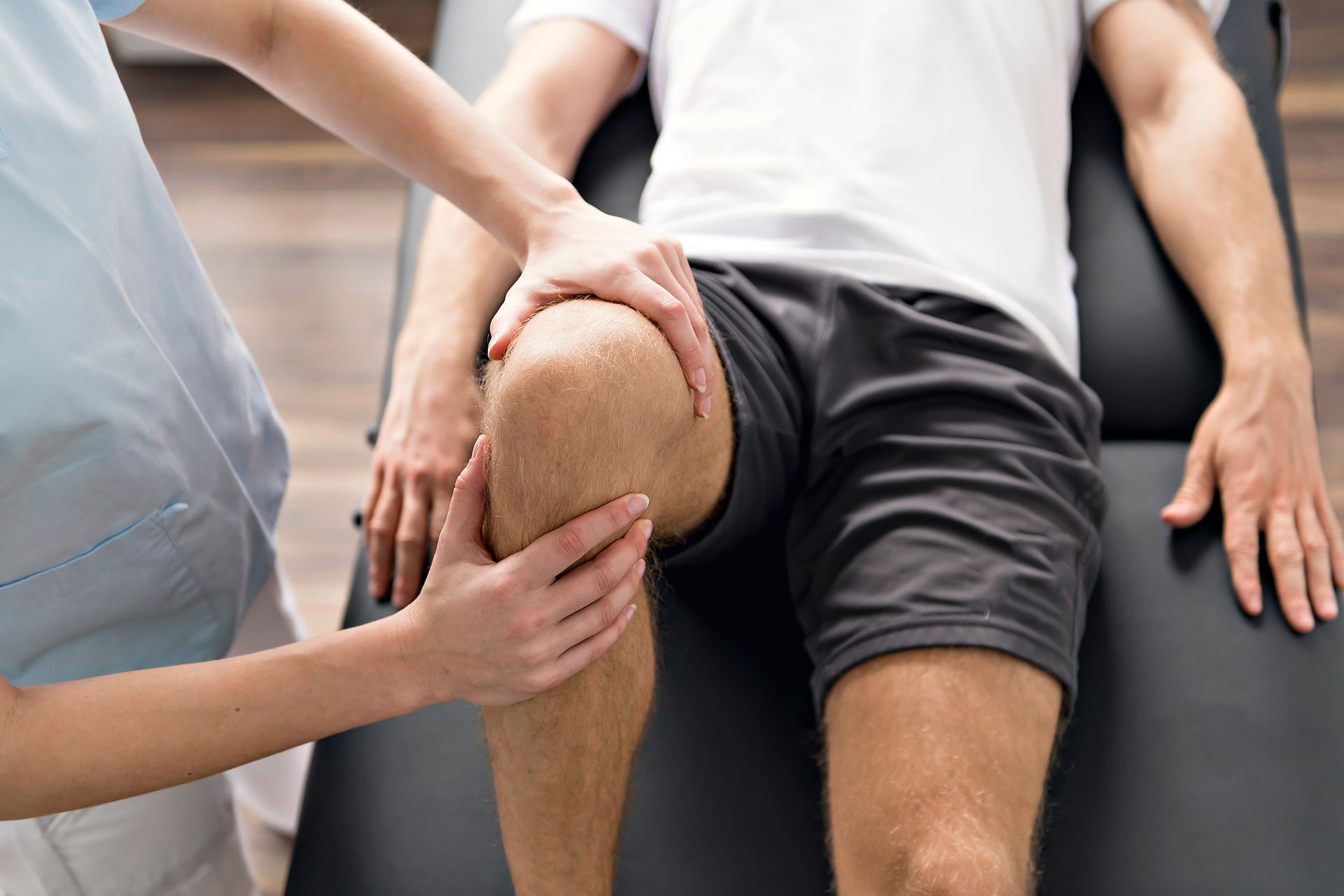 Physical therapist examining a patient’s knee while they sit on an exam table