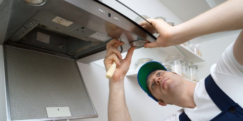 Technician repairing a stainless steel appliance under a counter with a wrench