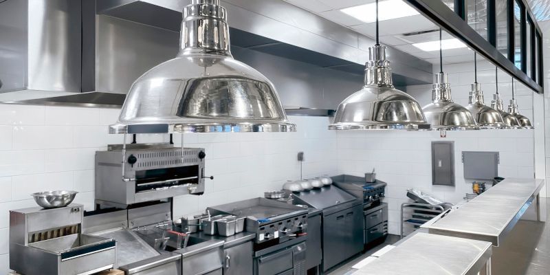 Modern stainless-steel restaurant kitchen with stoves, ovens, and overhead heat lamps