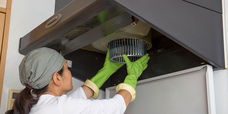 Person in green gloves cleaning a kitchen range hood filter in a modern kitchen