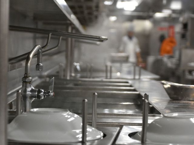 Stainless steel sinks in a commercial kitchen with blurred staff in the background