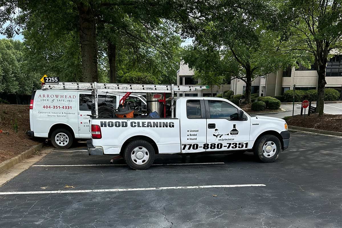 White utility truck with ladder racks and company logos parked in a tree-lined lot