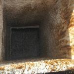 Dark square opening inside a rough brown stone or concrete shaft, viewed from above