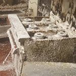 Stone fountain with water spraying into a basin, creating a wet, textured surface.