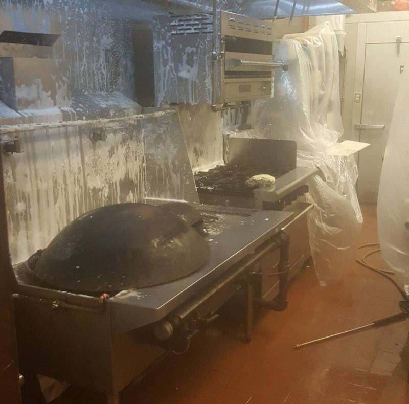 Fire-damaged commercial kitchen with smoke, a burnt stove, and overturned equipment, covered in soot and water