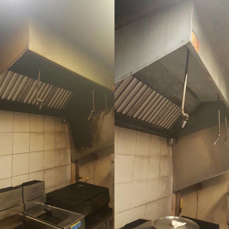 Commercial kitchen with stainless steel ventilation hoods above tiled walls and cooking equipment