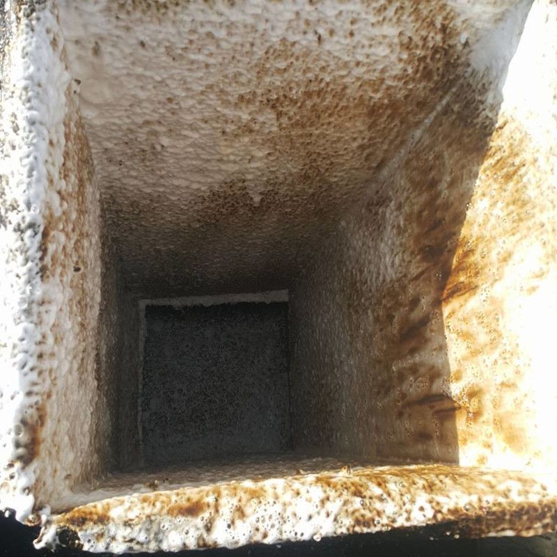 Rusty square metal chute opening with a dark interior.