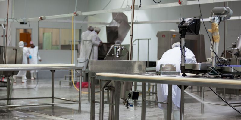 People in white lab coats working in a clean industrial lab with stainless steel equipment