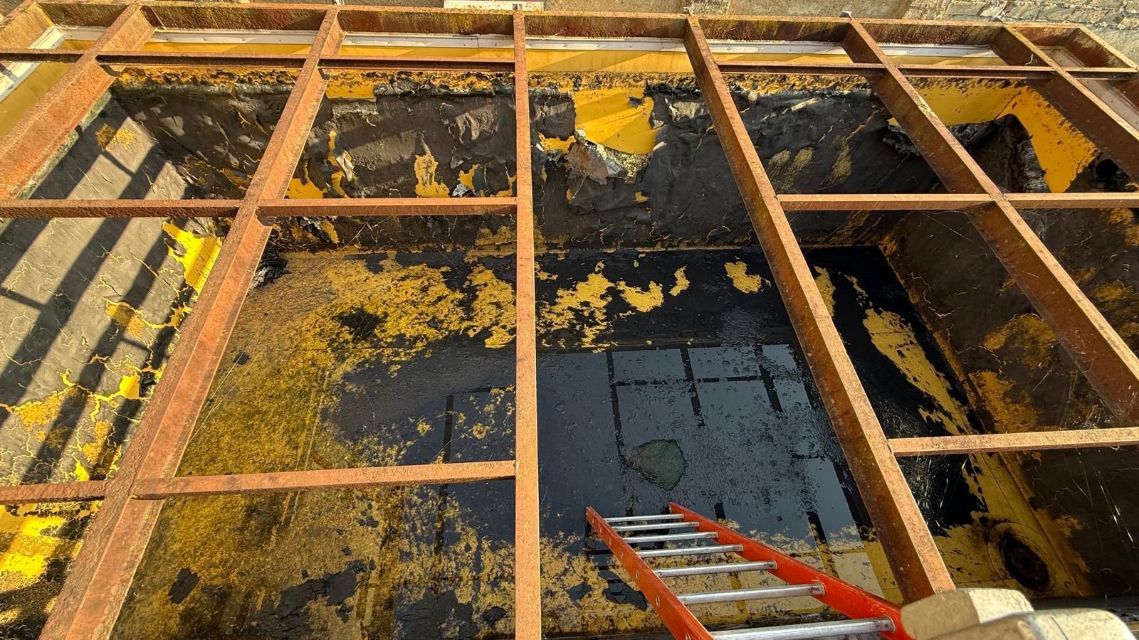 Tetto parzialmente demolito con travi di legno a vista, detriti e una scala rossa sottostante.