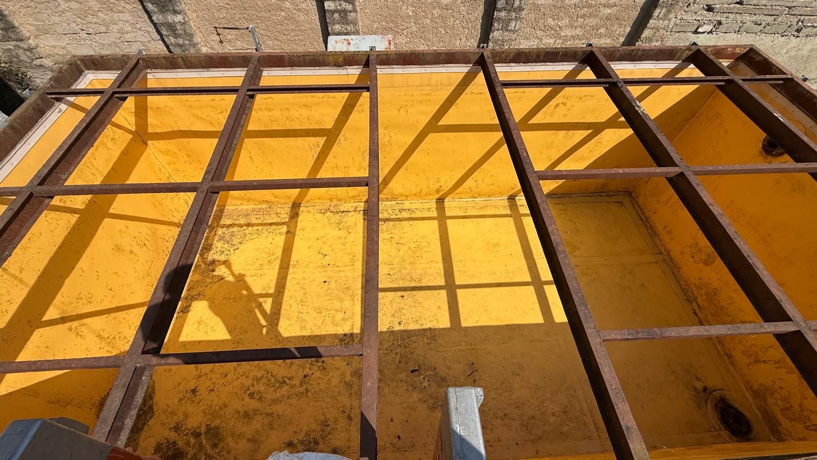 Impalcature metalliche arrugginite sopra un muro giallo illuminato dal sole o una superficie in costruzione