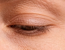 Close-up de um olho fechado com cílios longos e pele  com linhas de expressão.