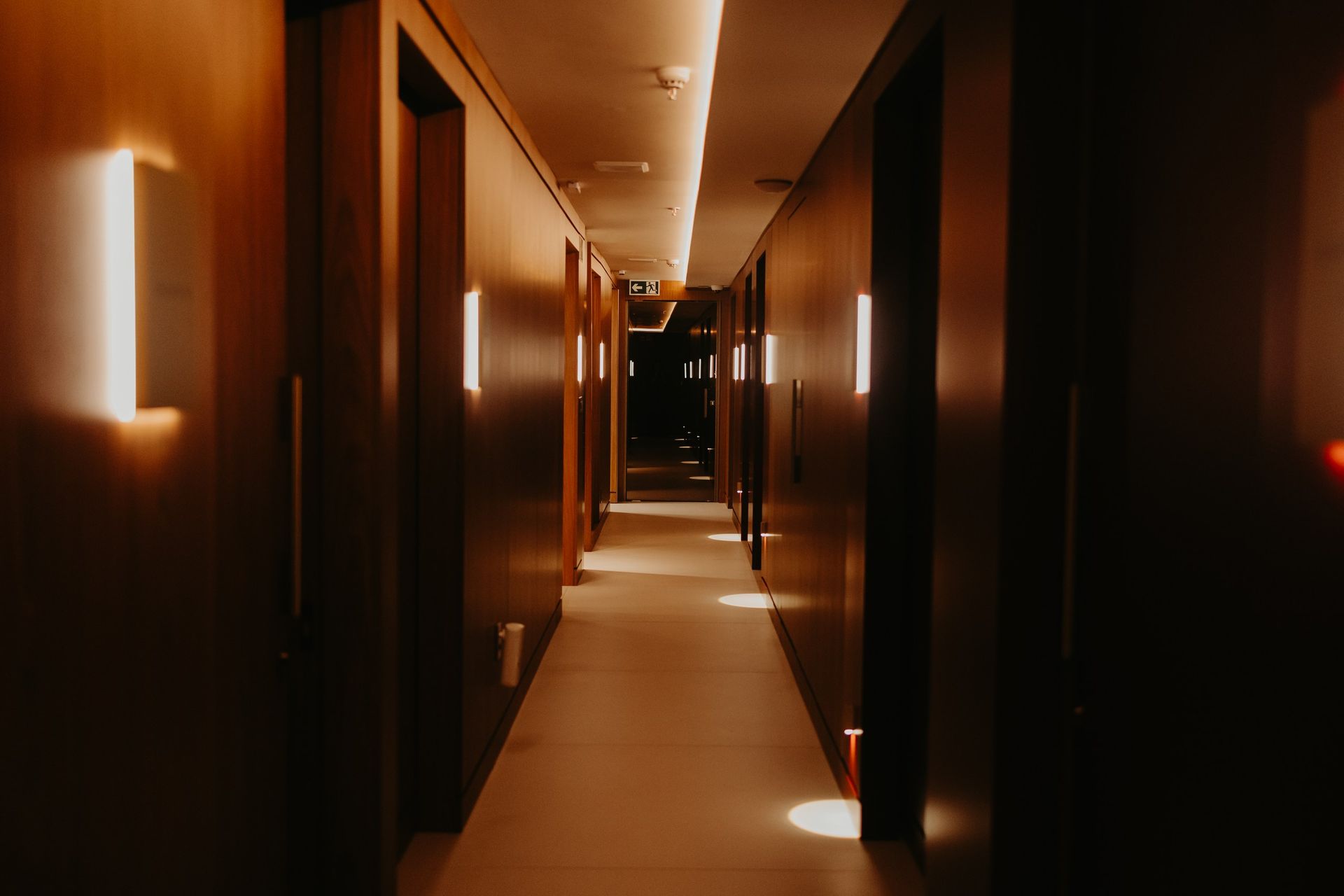 Corredor moderno e pouco iluminado com luminárias de parede em tons quentes e uma longa perspectiva de ponto de fuga.