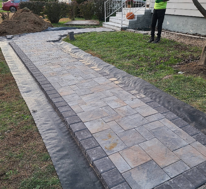 Newly paved stone walkway bordered by grass and soil in a residential yard.