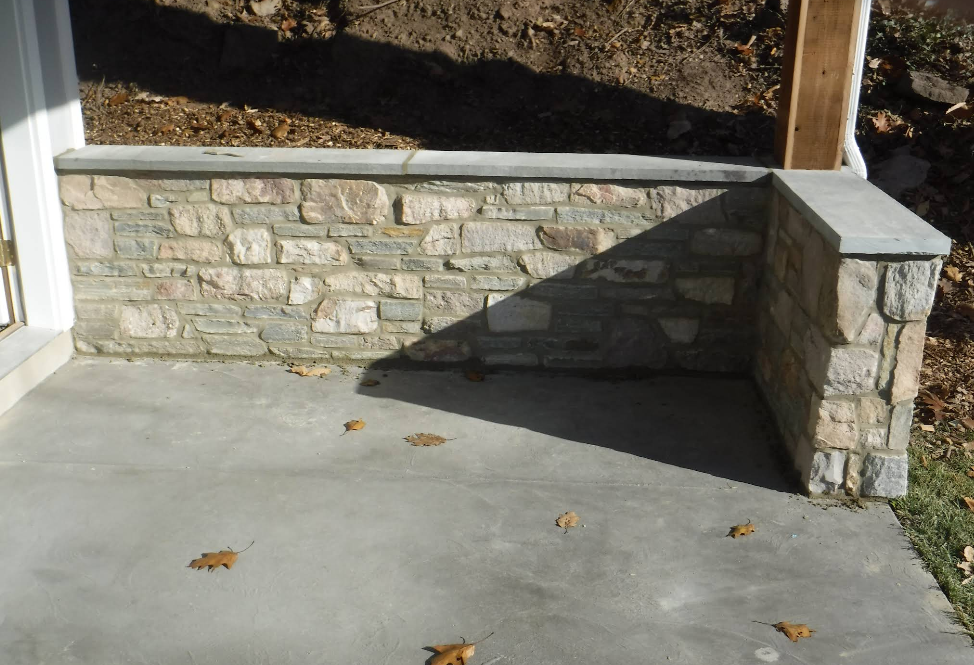 Stone retaining wall and concrete patio in front of a doorway, with fallen leaves and a small stone pillar.
