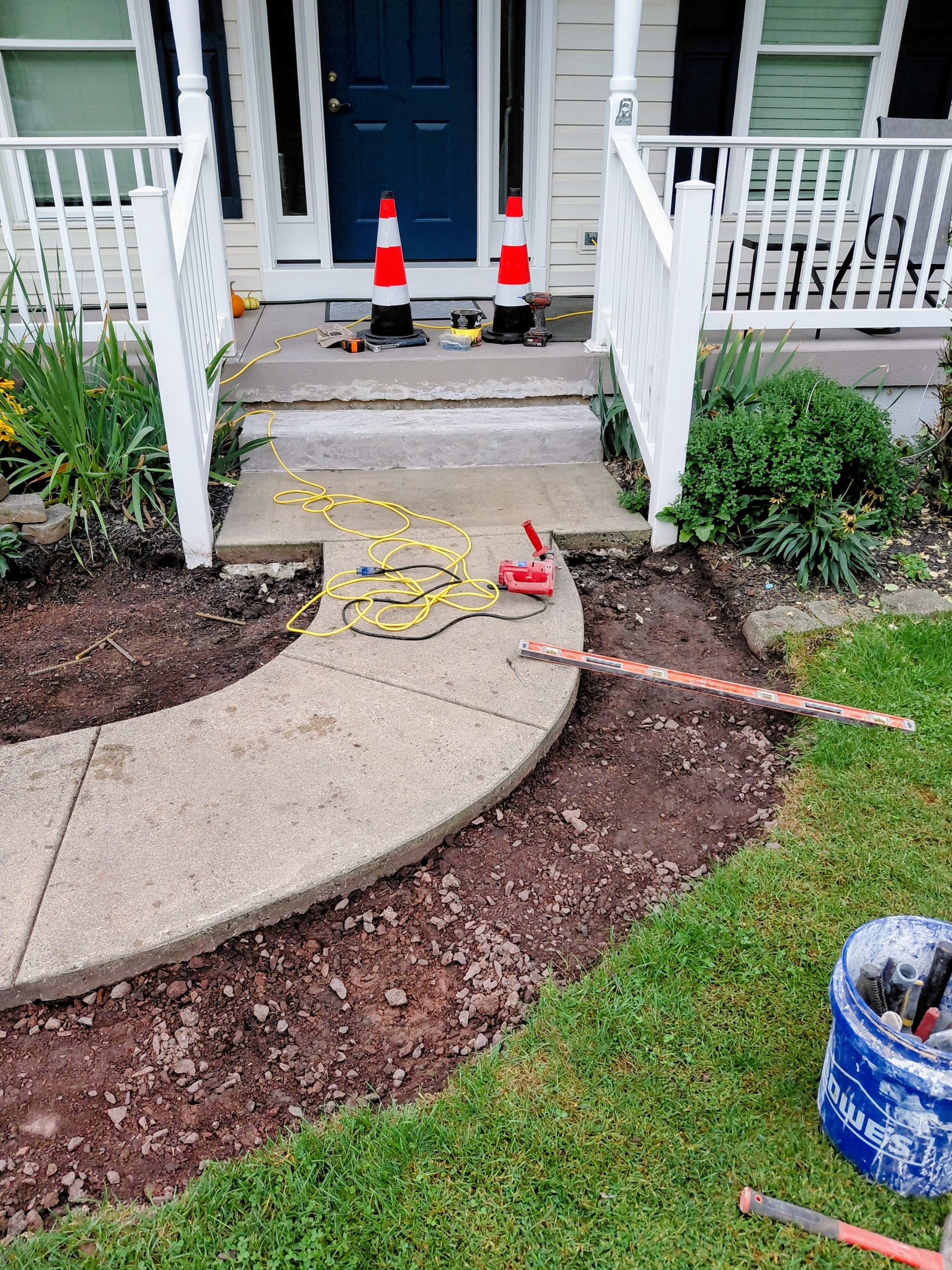 Before photo of a small backyard with a brick path, patchy grass, wooden fence, and shrubs
