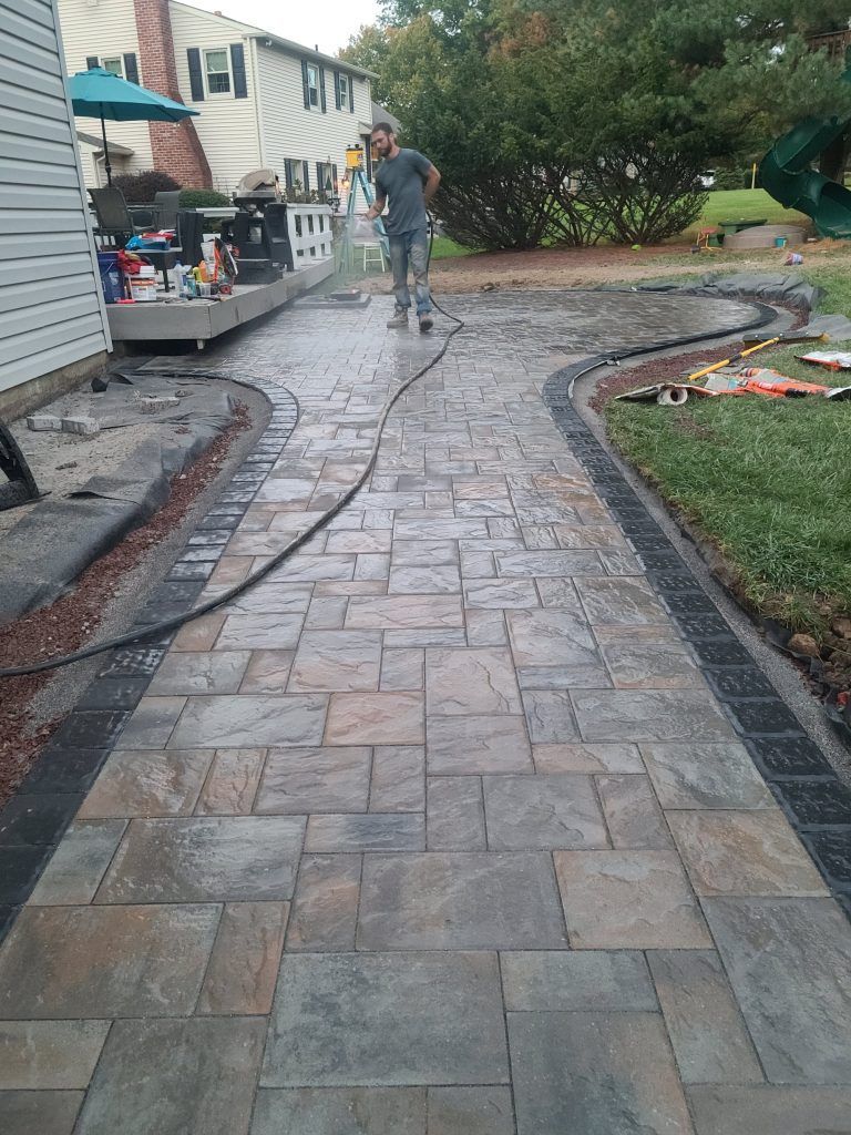 Stamped concrete walkway with curved garden border, leading past a house and patio area.
