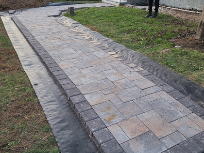 Newly paved brick walkway beside grass and a curb, with a person standing in the background